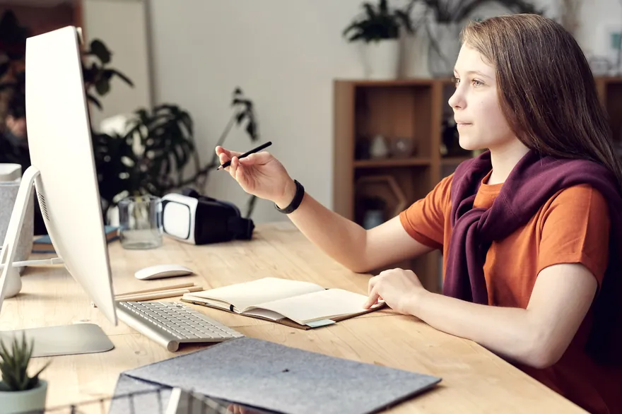A student working at a desk with a notebook and screen.