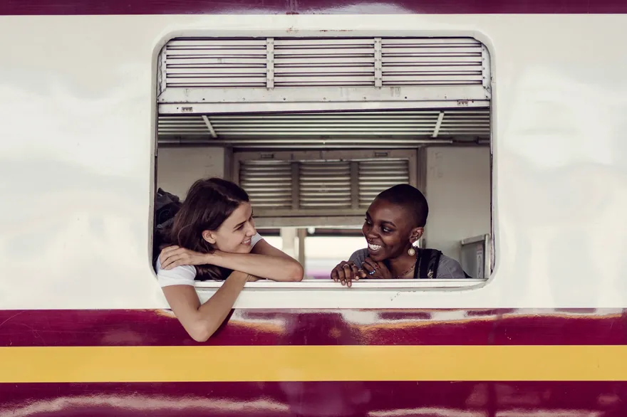 Two travellers leaning out of a train window, smiling.