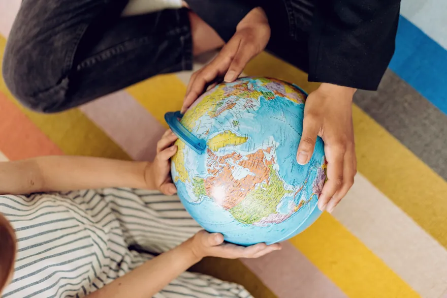Several hands together holding a small globe.