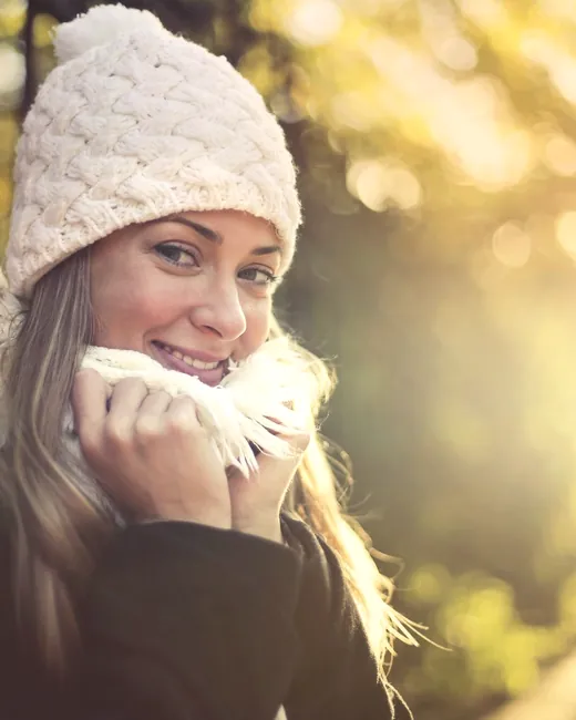 A young woman smiling warmly outdoors in golden afternoon light.