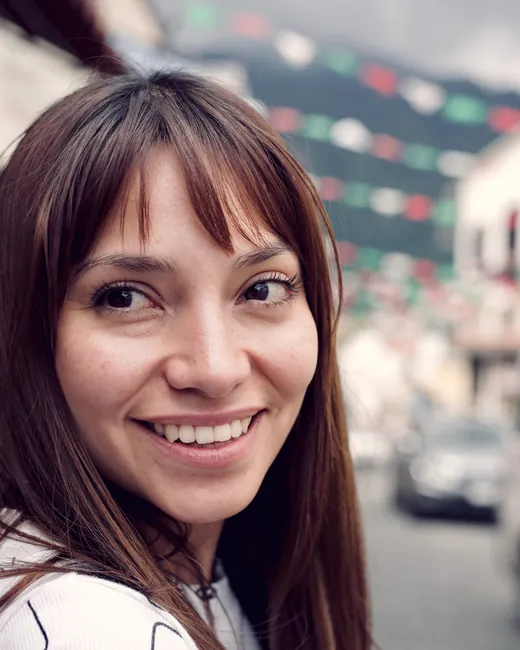 A young woman smiling on a street strung with festive lights.